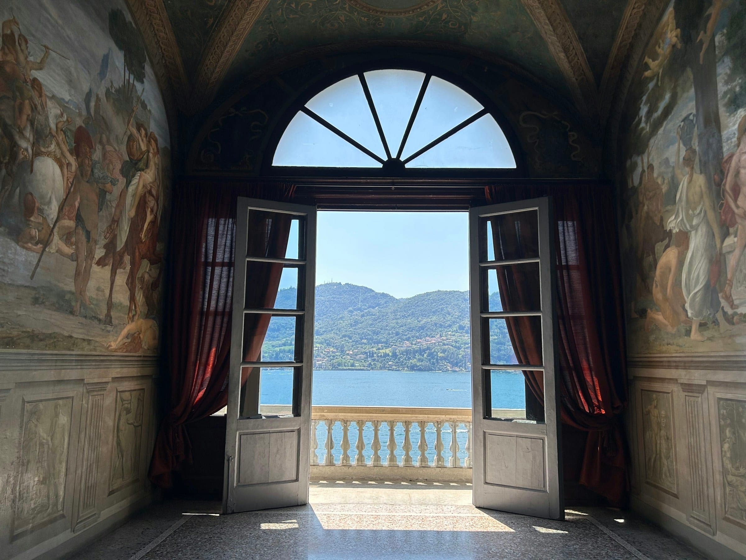 A frescoed room with tall doors open to the lake