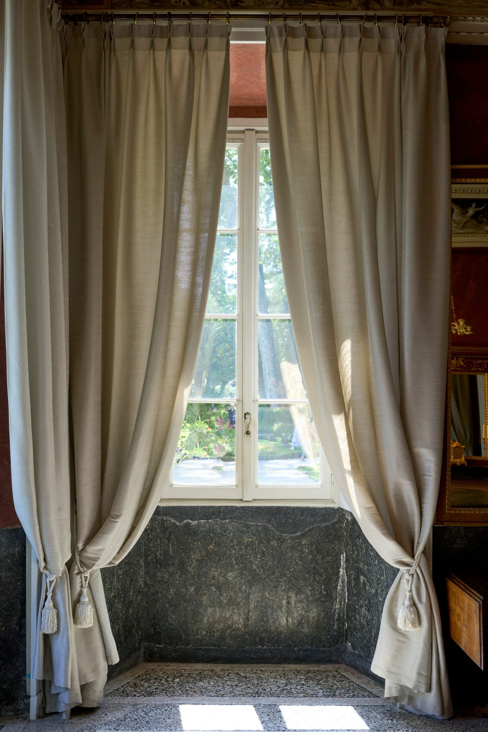 A window with tied-back linen curtains above a stone seat