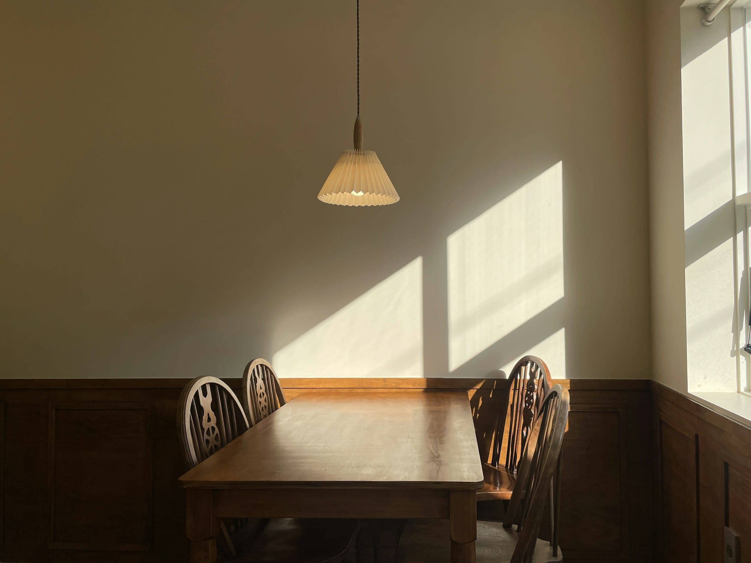 A wooden table under one pendant lamp, sun on a pale wall