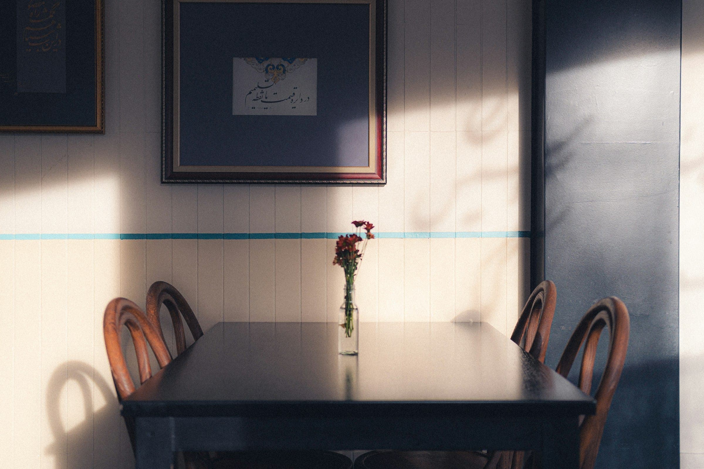 A dark table with red flowers in a glass, framed calligraphy above